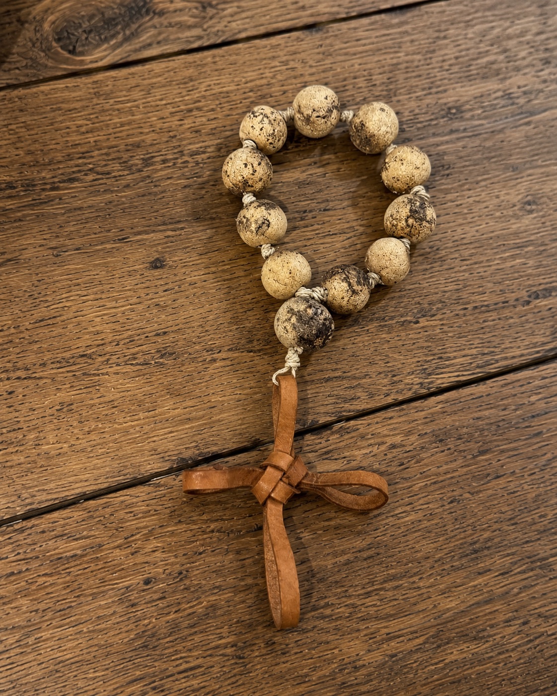 Decenario with coffee and clay mix beads and a woven leather cross on a wood surface