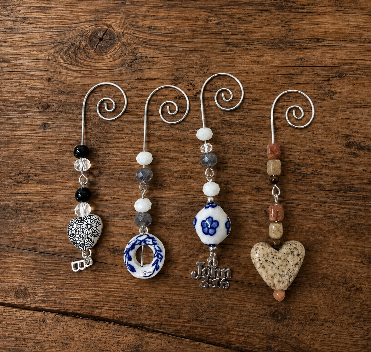 Four handmade tea bag charms with wire hooks, beads, and small charms on a wood surface
